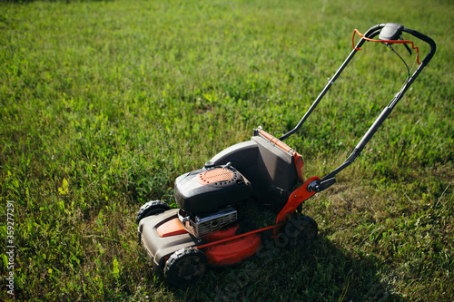 Close up of a red lawn mower cutting grass and lawn on nature at sunrise.