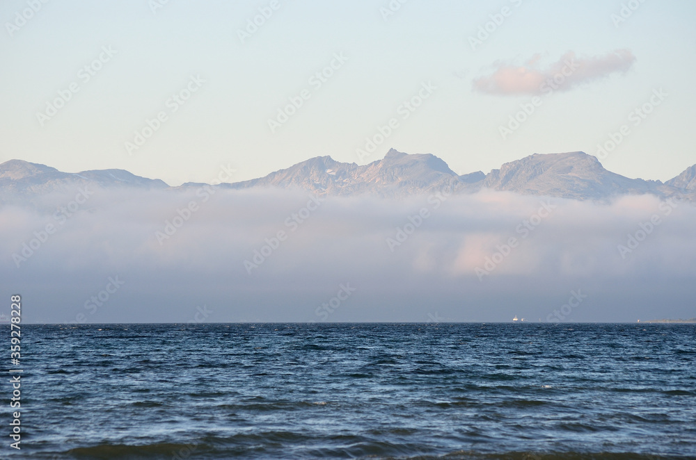 thick ocean fog and mountain range on blue sunny autumn day