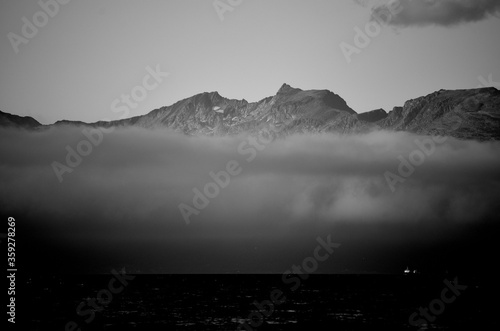 fog shrouded mountain range behind fjord and fishing boats