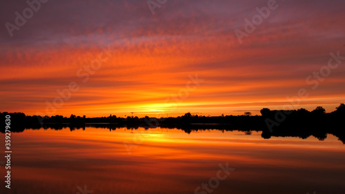 Symmetry of the sky in a lake at sunrise. Clouds reflecting on the water. Holiday landscape by the sea. Quiet relaxing scene with a beautiful colorful sky.