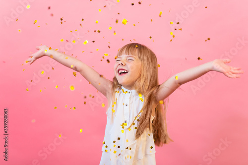 A little white girl is happy, confetti is showered on her, a holiday, a party, a greeting. on a pink background