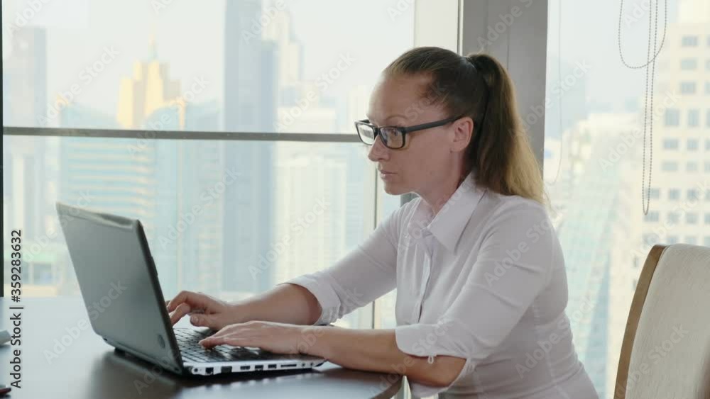 woman works on computer in office with panoramic windows with view business city. woman works on computer in office with panoramic windows with view business city.