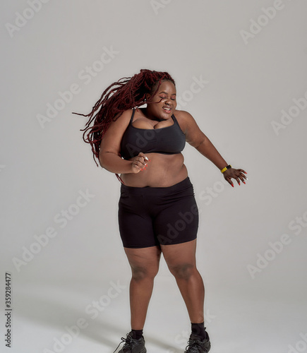 My body none of your business. Plump, plus size african american woman in sportswear having fun, dancing in studio over grey background photo