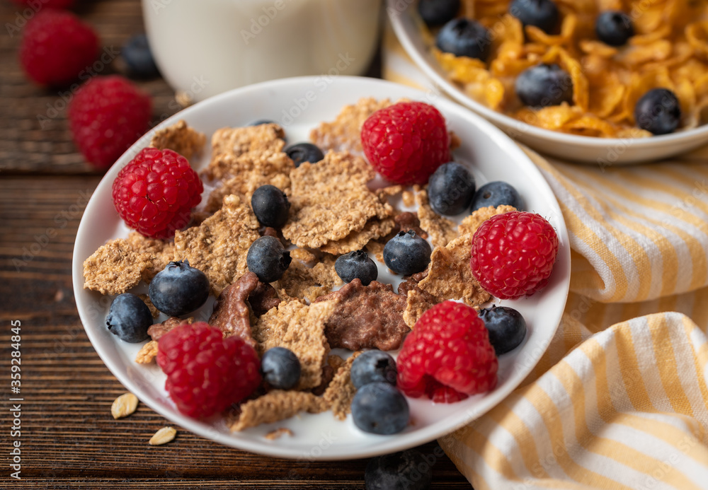 Corn flakes with blueberries and raspberries in white bowl in dark wooden desk. Corn flakes with blueberries and raspberries in white bowl in dark wooden desk.