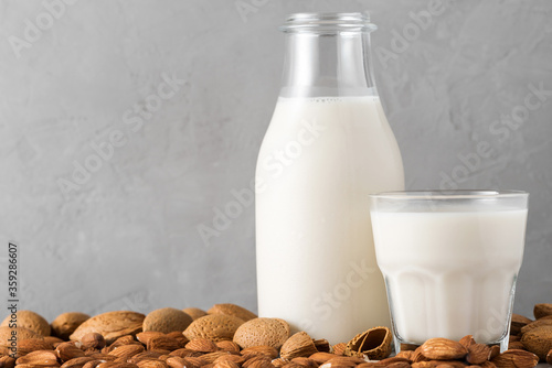 Plant based almond vegan milk in a bottle with a glass of milk and nuts on concrete background. Dairy free milk