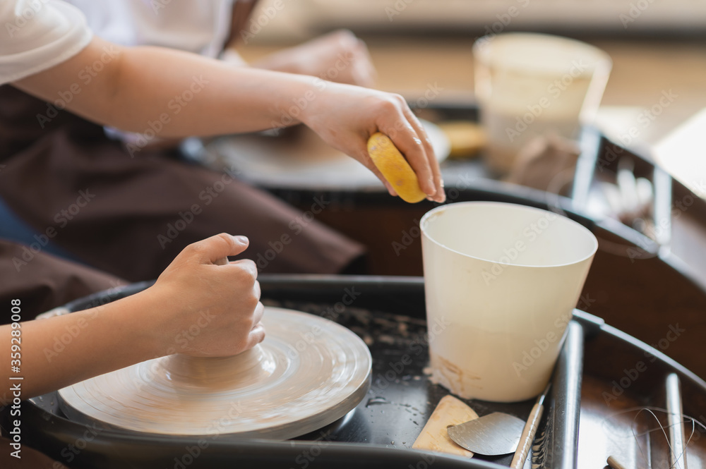 Female potter makes a pot on the pottery wheel close-up.