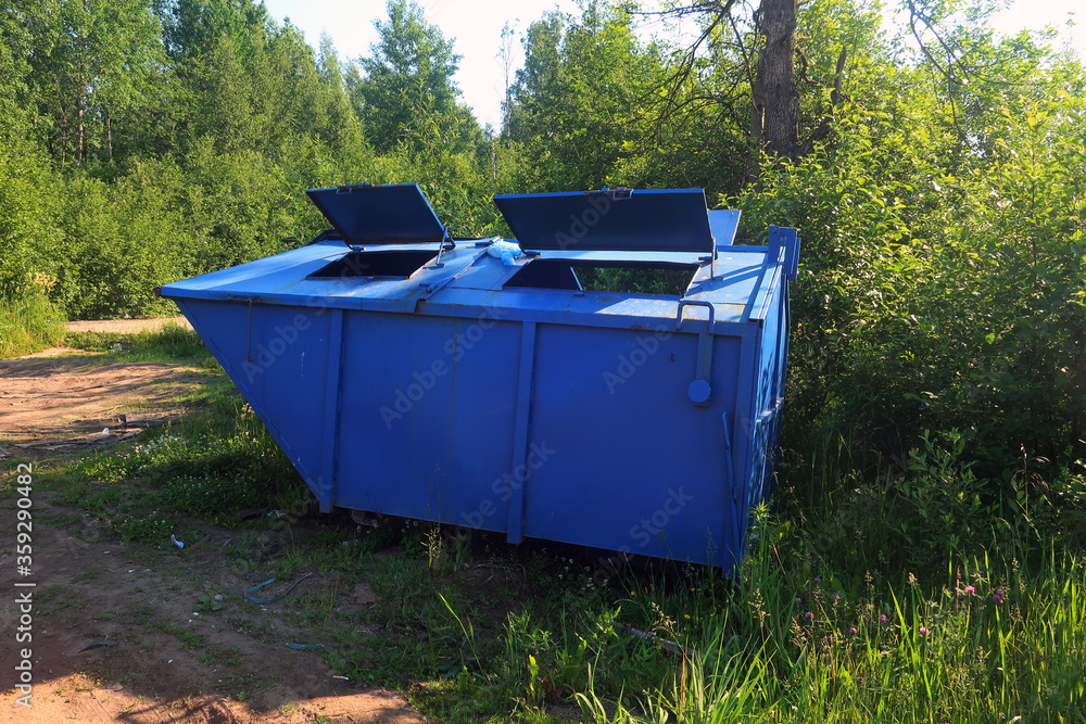 blue metal garbage container with open manhole covers in a clearing among trees blue metal garbage container with open manhole covers in a clearing among trees