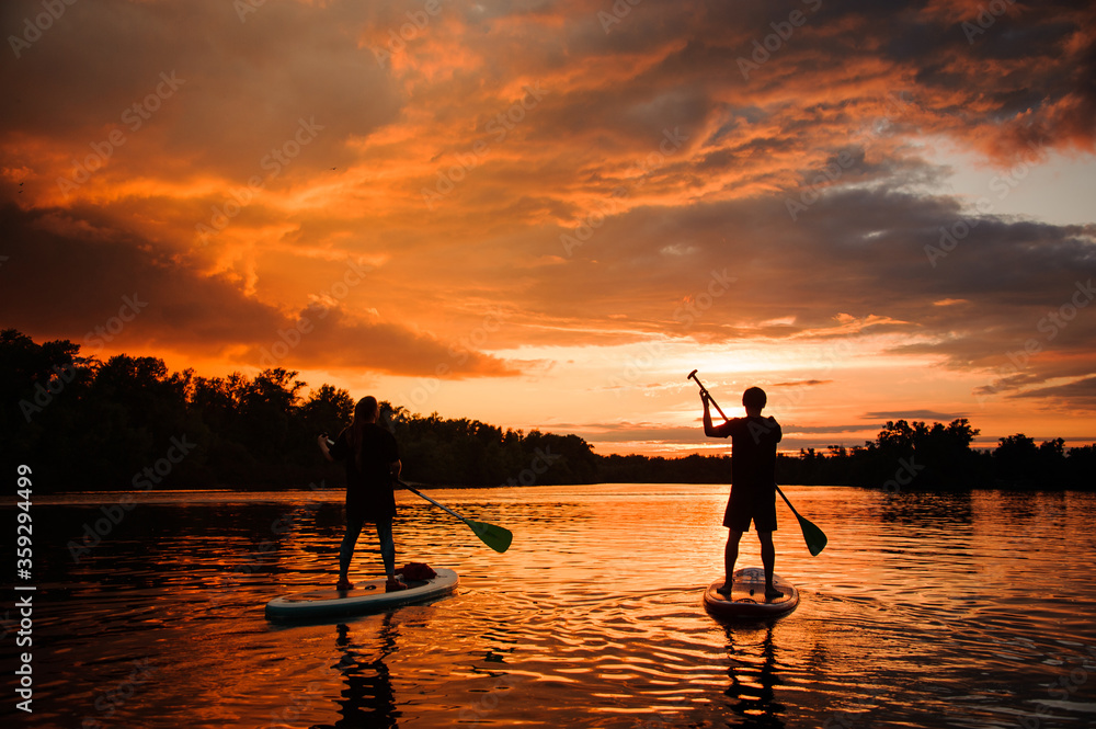 Beautiful rear view of two people on sup boards which floating on the river at sunset