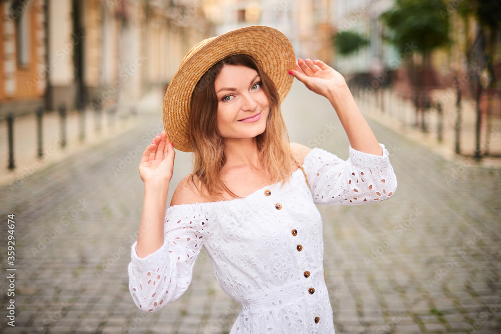 smiling girl walking on street in center of old town. woman in straw hat on summer trip in Europe