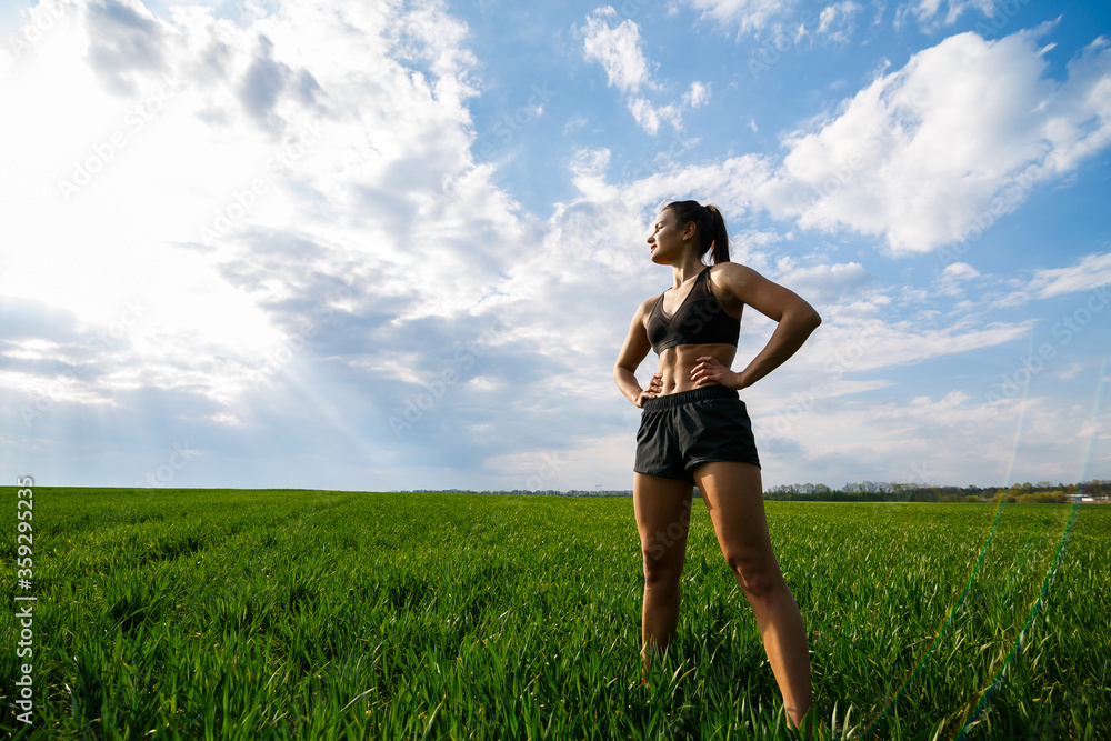 Girl athlete does warm-up outdoors, exercises for muscles. Young woman go in for sports, healthy lifestyle, athletic body. She is in sportswear, black top and shorts. Sport concept.