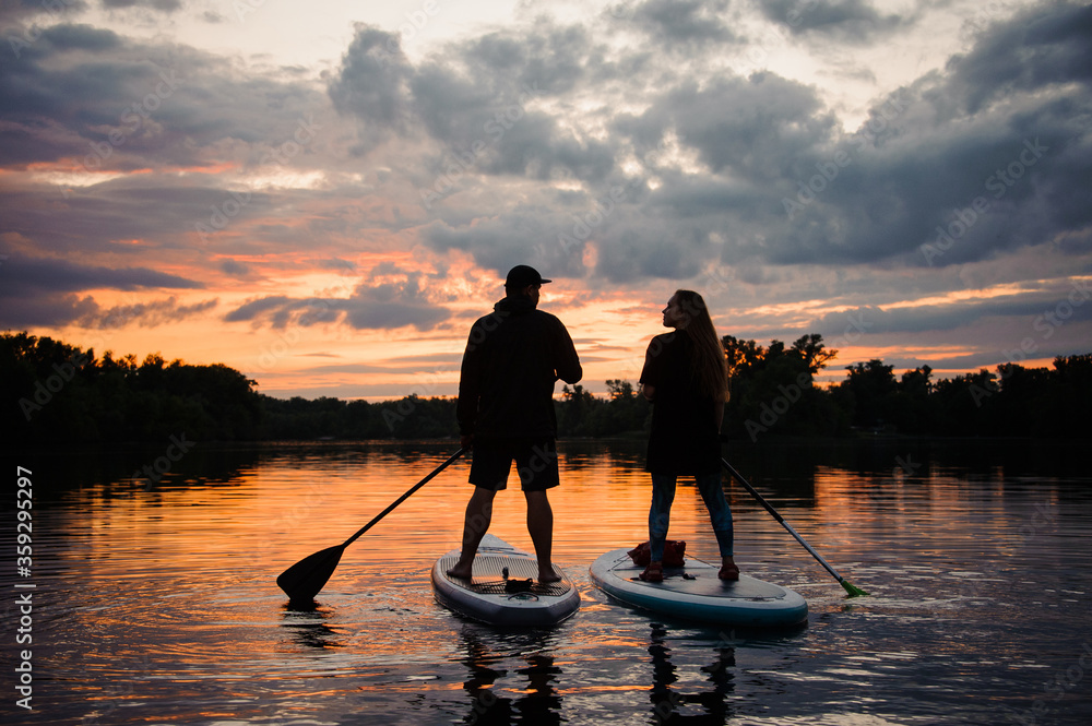 beautiful rear view on couple of people on sup boards on the river at sunset