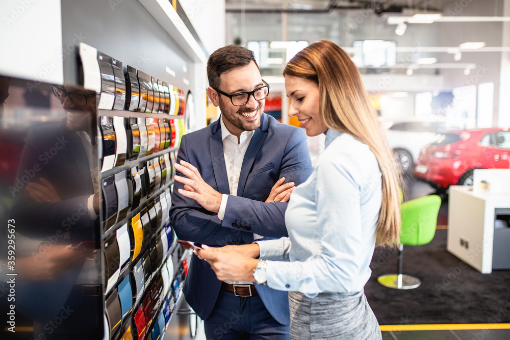 Young handsome man talking with saleswoman and choosing a color for his new car at car showroom. Young handsome man talking with saleswoman and choosing a color for his new car at car showroom.