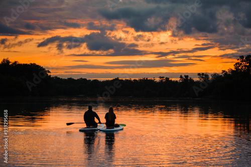 romantic rear view on couple of sitting people on sup boards on the river at sunset