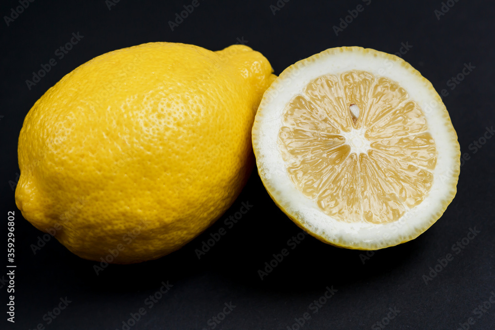 One whole lemon and one half lemon isolated on a black background.