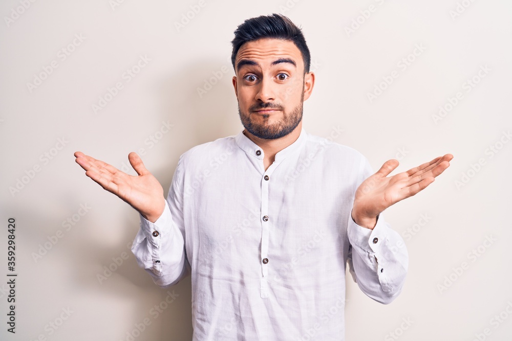 Young handsome man with beard wearing casual t-shirt standing over white background clueless and confused with open arms, no idea and doubtful face. Young handsome man with beard wearing casual t-shirt standing over white background clueless and confused with open arms, no idea and doubtful face.