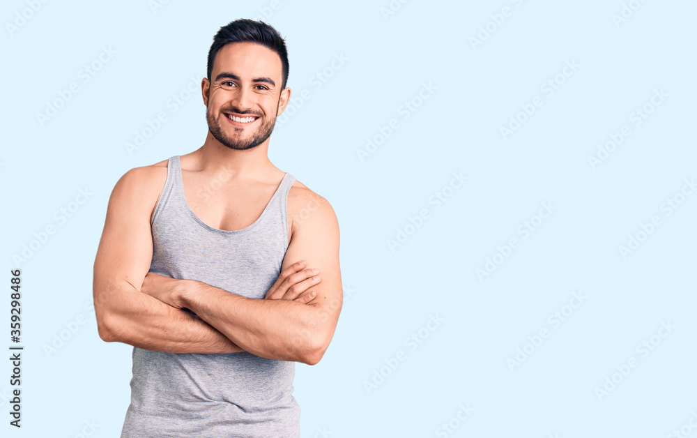 Young handsome man wearing swimwear and sleeveless t-shirt happy face smiling with crossed arms looking at the camera. positive person. Young handsome man wearing swimwear and sleeveless t-shirt happy face smiling with crossed arms looking at the camera. positive person.