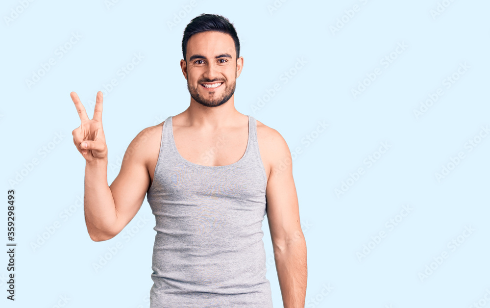 Naklejka premium Young handsome man wearing swimwear and sleeveless t-shirt showing and pointing up with fingers number two while smiling confident and happy.