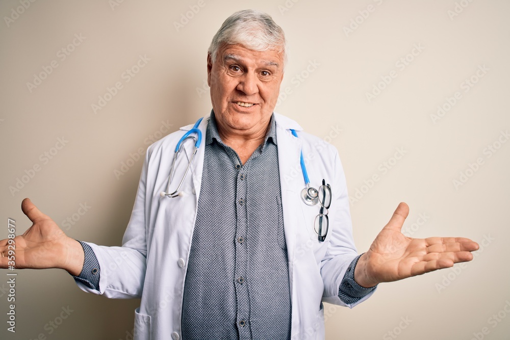 Senior handsome hoary doctor man wearing coat and stethoscope over white background clueless and confused expression with arms and hands raised. Doubt concept. Senior handsome hoary doctor man wearing coat and stethoscope over white background clueless and confused expression with arms and hands raised. Doubt concept.