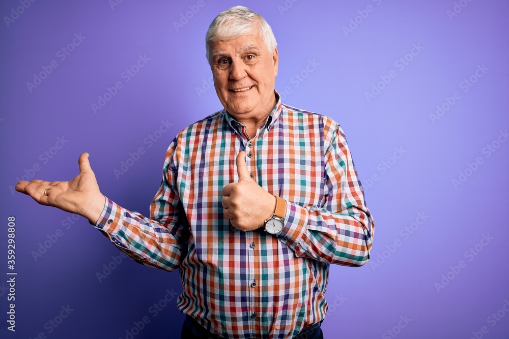 Naklejka premium Senior handsome hoary man wearing casual colorful shirt over isolated purple background Showing palm hand and doing ok gesture with thumbs up, smiling happy and cheerful