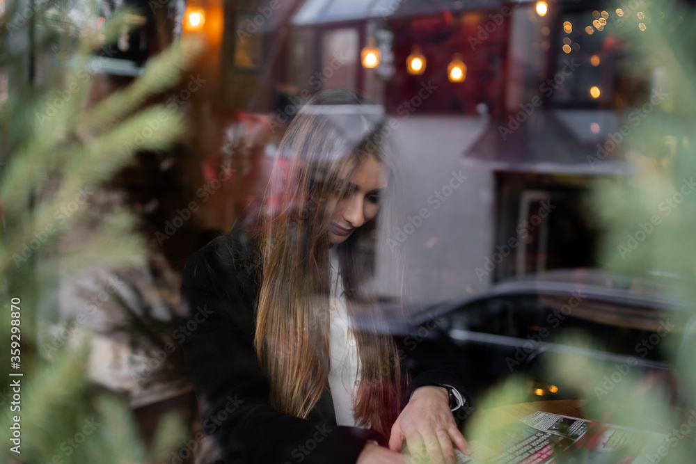 Beautiful brunette girl behind the glass, portrait of young woman in window, concept of female emotions. female model looking through the window. Winter cafe concept.