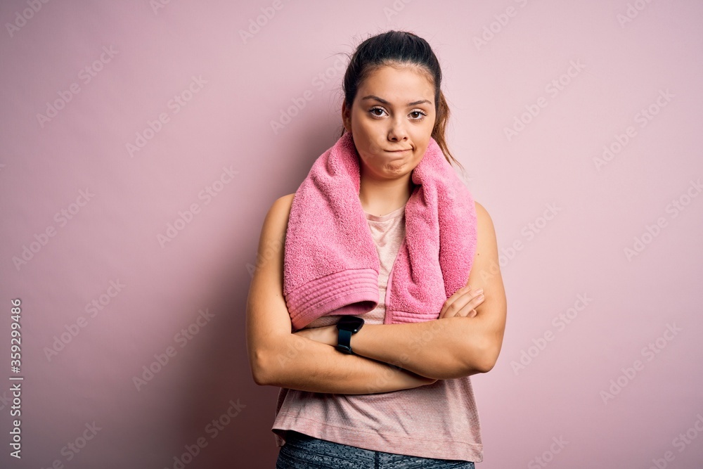 Young beautiful brunette sportswoman wearing sportswear and towel over pink background skeptic and nervous, disapproving expression on face with crossed arms. Negative person. Young beautiful brunette sportswoman wearing sportswear and towel over pink background skeptic and nervous, disapproving expression on face with crossed arms. Negative person.