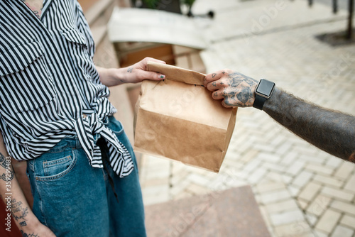 Close up of hands and paper bag. Delivery man giving away order to a female customer, while delivering food. Courier, delivery service concept