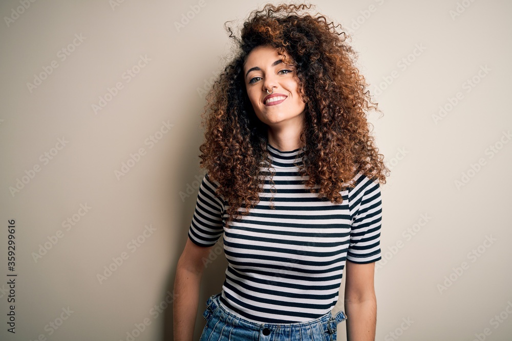 Young beautiful woman with curly hair and piercing wearing casual striped t-shirt with a happy and cool smile on face. Lucky person. Young beautiful woman with curly hair and piercing wearing casual striped t-shirt with a happy and cool smile on face. Lucky person.