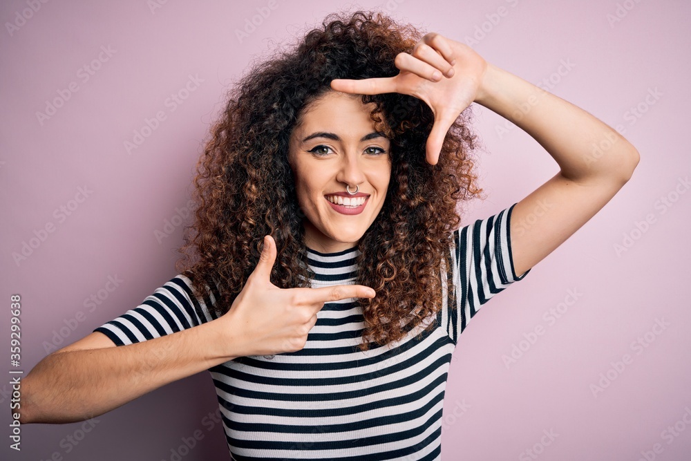 Young beautiful woman with curly hair and piercing wearing casual striped t-shirt smiling making frame with hands and fingers with happy face. Creativity and photography concept. Young beautiful woman with curly hair and piercing wearing casual striped t-shirt smiling making frame with hands and fingers with happy face. Creativity and photography concept.