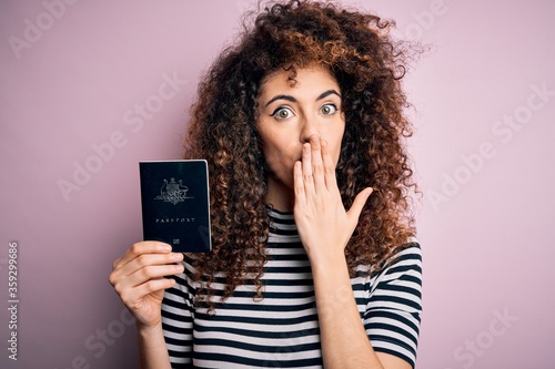 Beautiful tourist woman with curly hair and piercing holding australia australian passport id cover mouth with hand shocked with shame for mistake, expression of fear, scared in silence