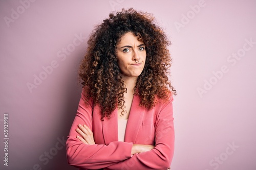 Young beautiful businesswoman with curly hair and piercing wearing elegant jacket skeptic and nervous, disapproving expression on face with crossed arms. Negative person.