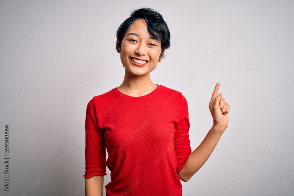 Young beautiful asian girl wearing casual red t-shirt standing over isolated white background with a big smile on face, pointing with hand finger to the side looking at the camera. Young beautiful asian girl wearing casual red t-shirt standing over isolated white background with a big smile on face, pointing with hand finger to the side looking at the camera.