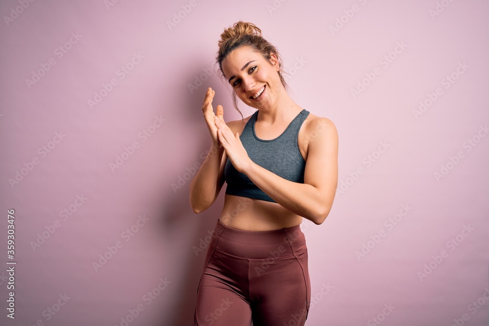 Young beautiful blonde sportswoman doing sport wearing sportswear over pink background clapping and applauding happy and joyful, smiling proud hands together Young beautiful blonde sportswoman doing sport wearing sportswear over pink background clapping and applauding happy and joyful, smiling proud hands together