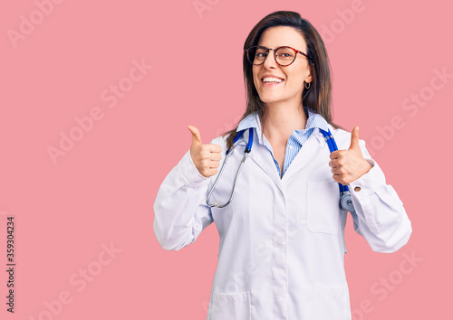 Young beautiful woman wearing doctor stethoscope and glasses success sign doing positive gesture with hand  thumbs up smiling and happy. cheerful expression and winner gesture.