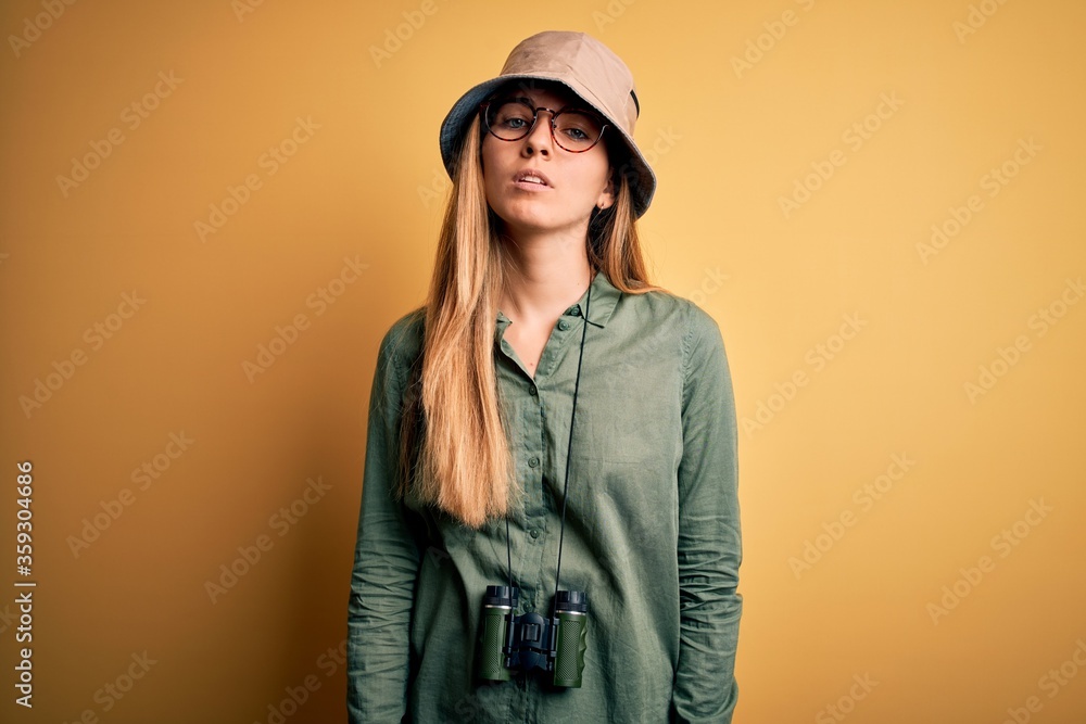 Beautiful blonde explorer woman with blue eyes wearing hat and glasses using binoculars Relaxed with serious expression on face. Simple and natural looking at the camera. Beautiful blonde explorer woman with blue eyes wearing hat and glasses using binoculars Relaxed with serious expression on face. Simple and natural looking at the camera.