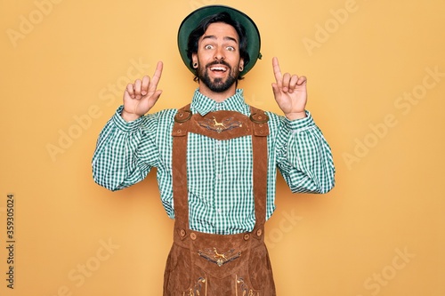 Young handsome man wearing tratidional german octoberfest custome for Germany festival smiling amazed and surprised and pointing up with fingers and raised arms.