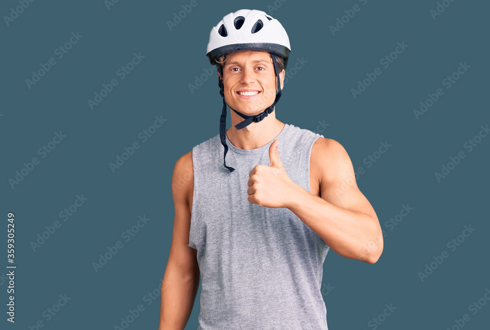 Young handsome man wearing bike helmet doing happy thumbs up gesture with hand. approving expression looking at the camera showing success. Young handsome man wearing bike helmet doing happy thumbs up gesture with hand. approving expression looking at the camera showing success.