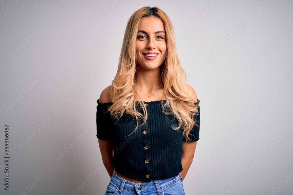 Young beautiful blonde woman wearing casual t-shirt standing over isolated white background with a happy and cool smile on face. Lucky person. Young beautiful blonde woman wearing casual t-shirt standing over isolated white background with a happy and cool smile on face. Lucky person.