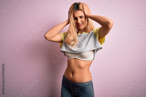 Young beautiful blonde sportswoman doing sport wearing sportswear over pink background suffering from headache desperate and stressed because pain and migraine. Hands on head.