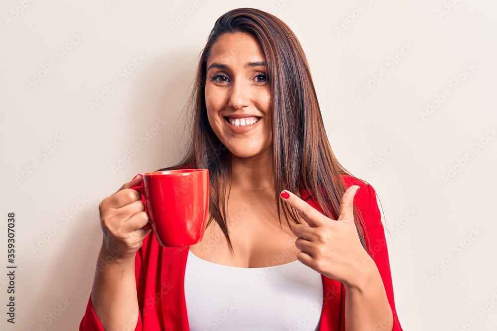 Young beautiful brunette woman drinking mug of coffee smiling happy pointing with hand and finger Young beautiful brunette woman drinking mug of coffee smiling happy pointing with hand and finger