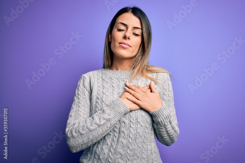 Young beautiful woman wearing casual sweater standing over isolated purple background smiling with hands on chest with closed eyes and grateful gesture on face. Health concept.