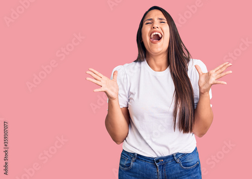 Young beautiful brunette woman wearing casual t-shirt celebrating mad and crazy for success with arms raised and closed eyes screaming excited. winner concept