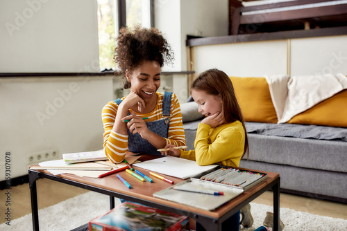 Experience childcare as it should be. Caucasian little girl spending time with african american baby sitter. They are drawing, learning how to draw, sitting on the floor