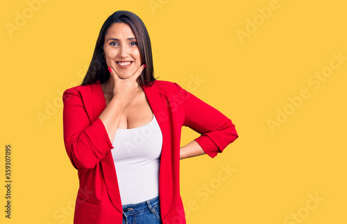 Young beautiful brunette woman wearing elegant clothes looking confident at the camera smiling with crossed arms and hand raised on chin. thinking positive.