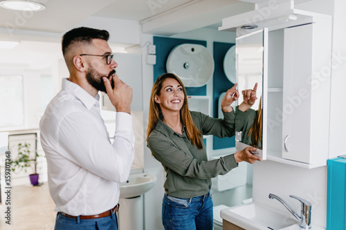 Middle age man choosing ceramic tiles and utensils for his home bathroom and female seller helps him to make right decision