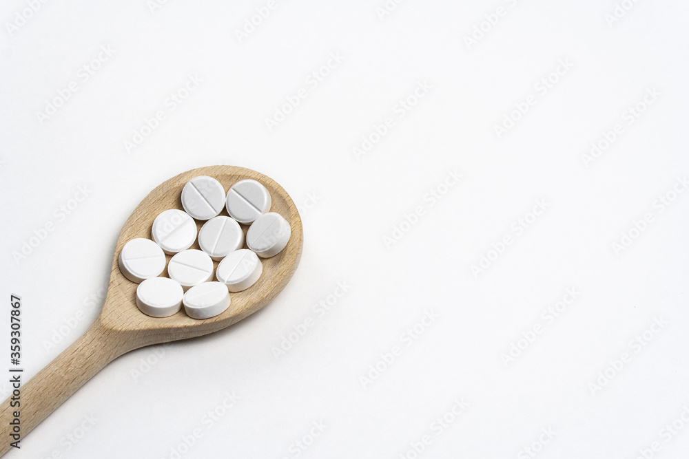 Wooden spoon with round tablets on white background isolated on left below side. Medications on table for coronavirus and pandemic, close up. Free space for text. Pills and drugs. Top view Macro shot Wooden spoon with round tablets on white background isolated on left below side. Medications on table for coronavirus and pandemic, close up. Free space for text. Pills and drugs. Top view Macro shot