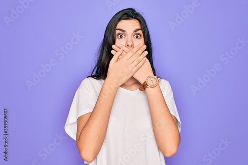 Young beautiful brunette woman wearing casual white t-shirt over purple background shocked covering mouth with hands for mistake. Secret concept.