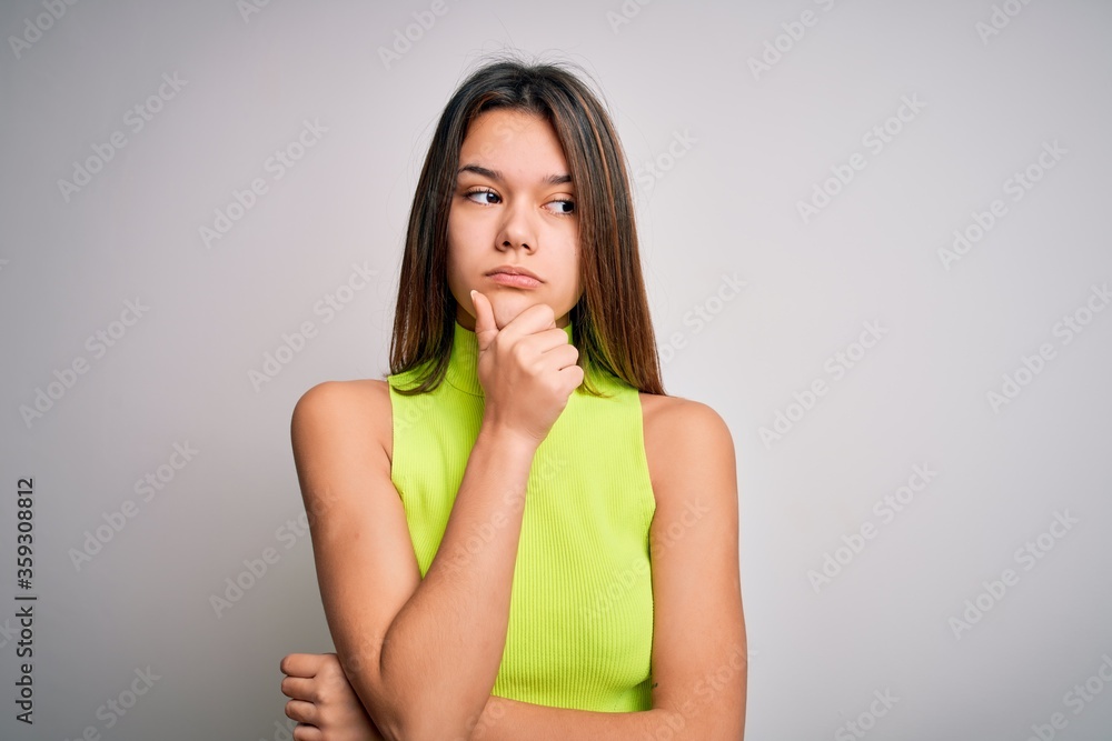 Young beautiful brunette girl wearing casual summer t-shirt over isolated white background with hand on chin thinking about question, pensive expression. Smiling with thoughtful face. Doubt concept. Young beautiful brunette girl wearing casual summer t-shirt over isolated white background with hand on chin thinking about question, pensive expression. Smiling with thoughtful face. Doubt concept.