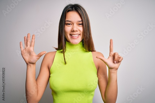 Young beautiful brunette girl wearing casual summer t-shirt over isolated white background showing and pointing up with fingers number seven while smiling confident and happy.