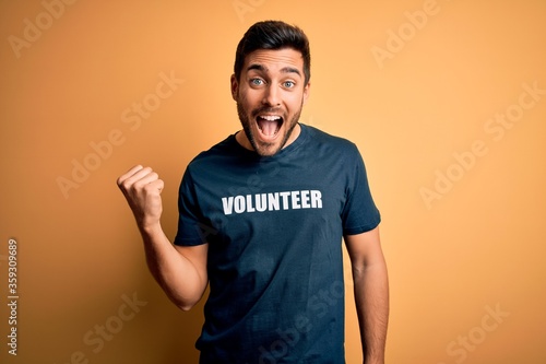 Young handsome man with beard volunteering wearing t-shirt with volunteer message screaming proud and celebrating victory and success very excited, cheering emotion © Krakenimages.com