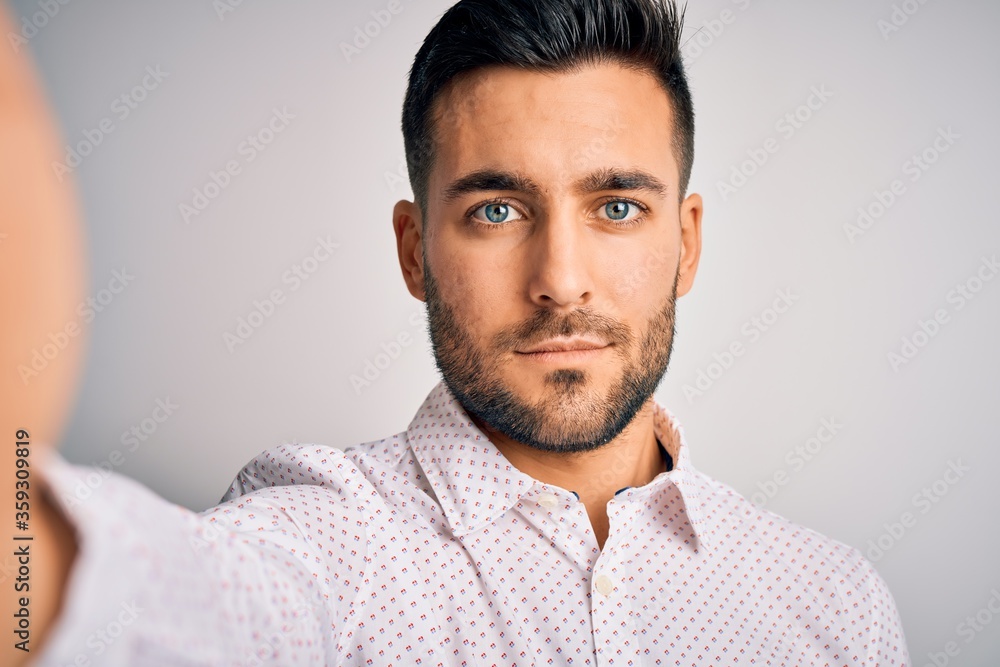 Fototapeta premium Young handsome man wearing shirt making selfie by the camera over white background with a confident expression on smart face thinking serious